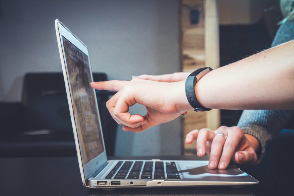A person gestures towards a laptop computer, indicating something on the screen with a focused expression.